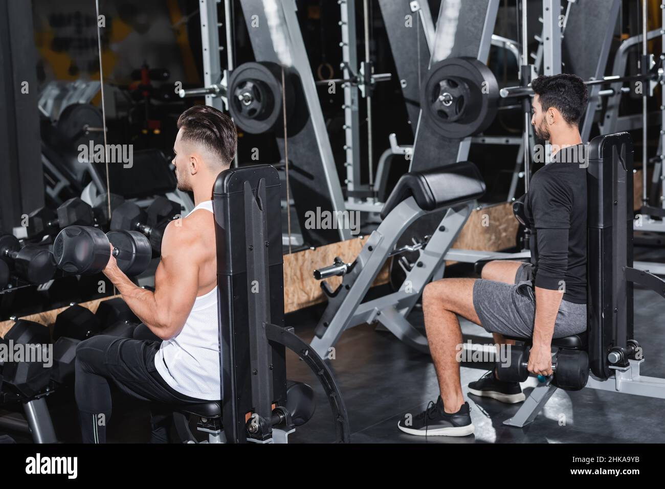 Sportivi multietnici allenati con manubri vicino a attrezzature sportive in palestra Foto Stock