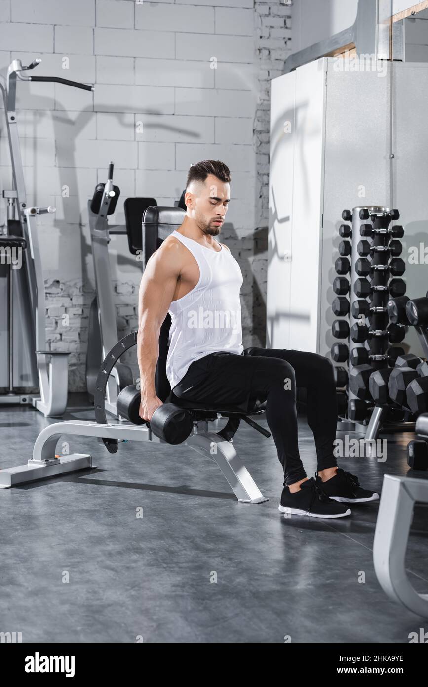 Atletico sportivo allenarsi con dumbbell vicino a attrezzature sportive in palestra Foto Stock