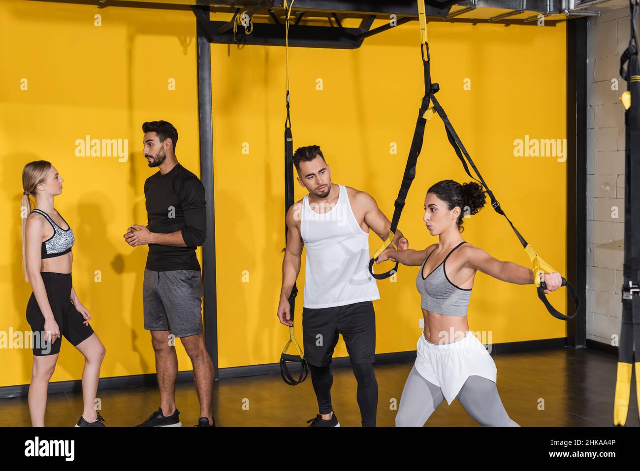 Medio Oriente sportswoman tirando le cinghie di sospensione vicino amici in palestra Foto Stock