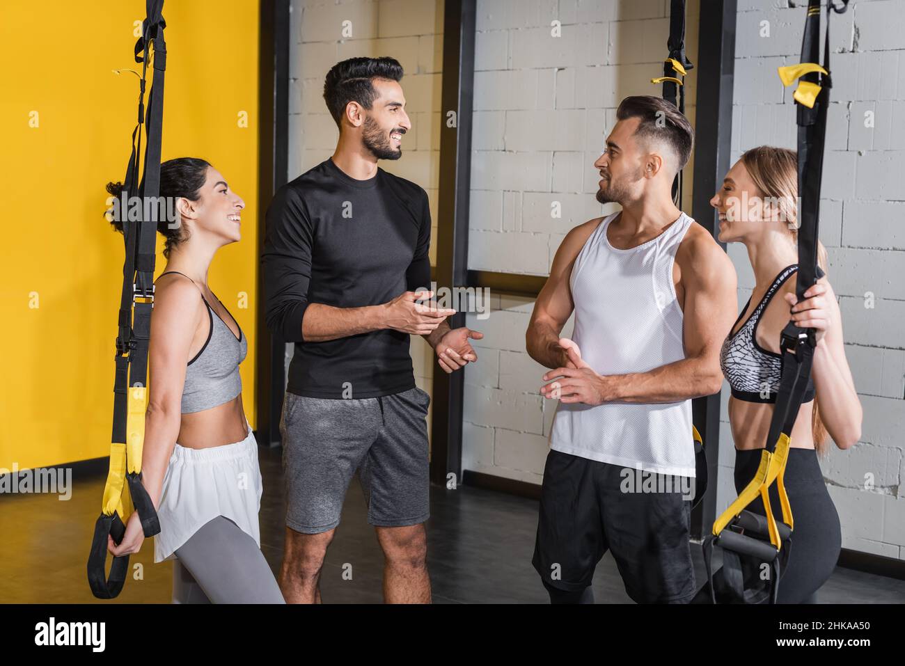 Sorridente gente interrazziale che parla vicino a cinghie di sospensione in palestra Foto Stock