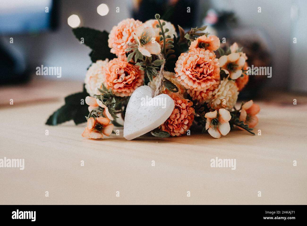 tavolo di legno con un bouquet di fiori e un cuore bianco e bokeh luci intorno ad esso. Foto Stock