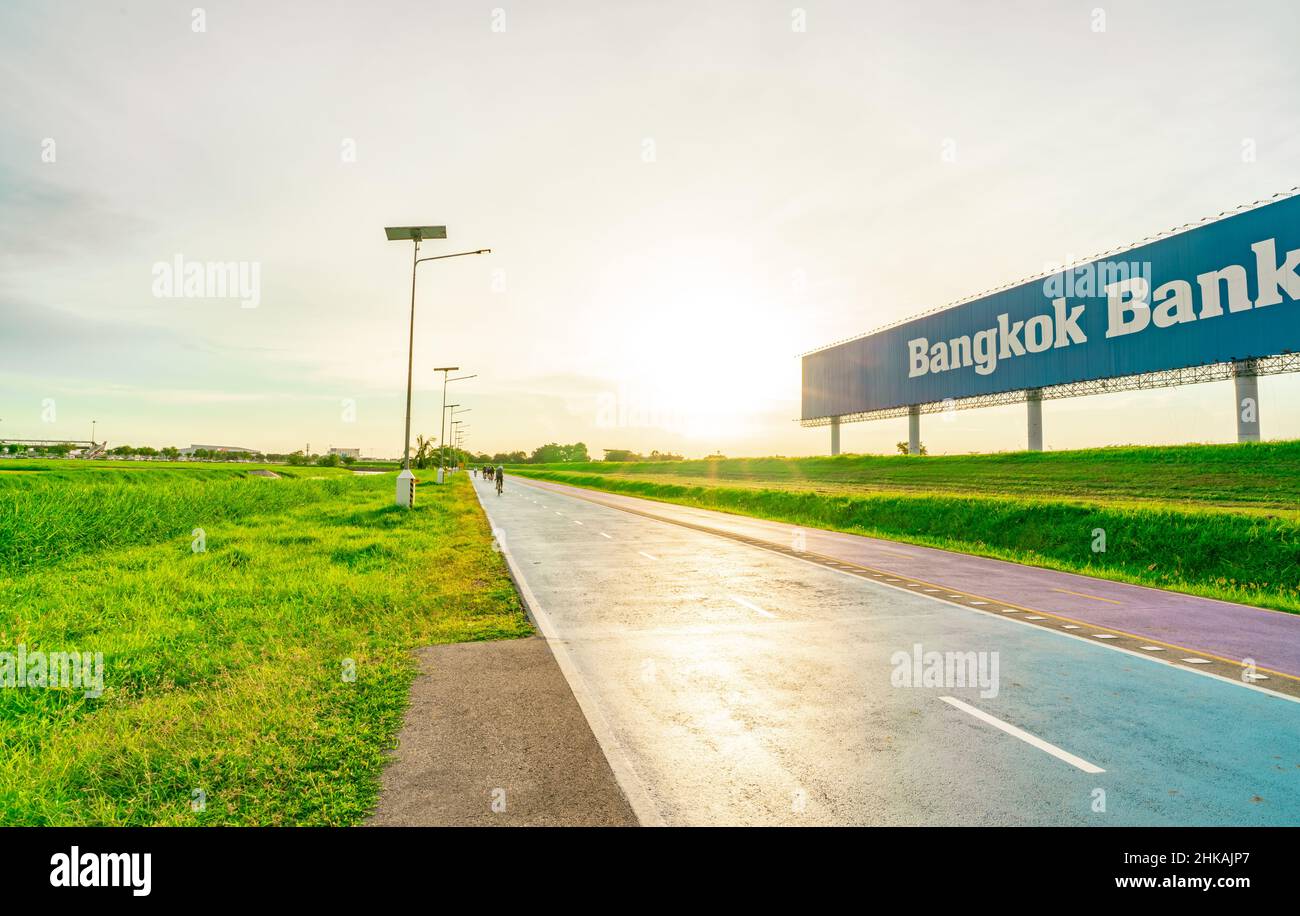 SAMUT PRAKAN, THAILANDIA-18 GIUGNO 2021 : Bangkok Banca pubblicità cartellone con cielo tramonto e verde erba. Sport uomo giro biciclette sulla strada. Foto Stock