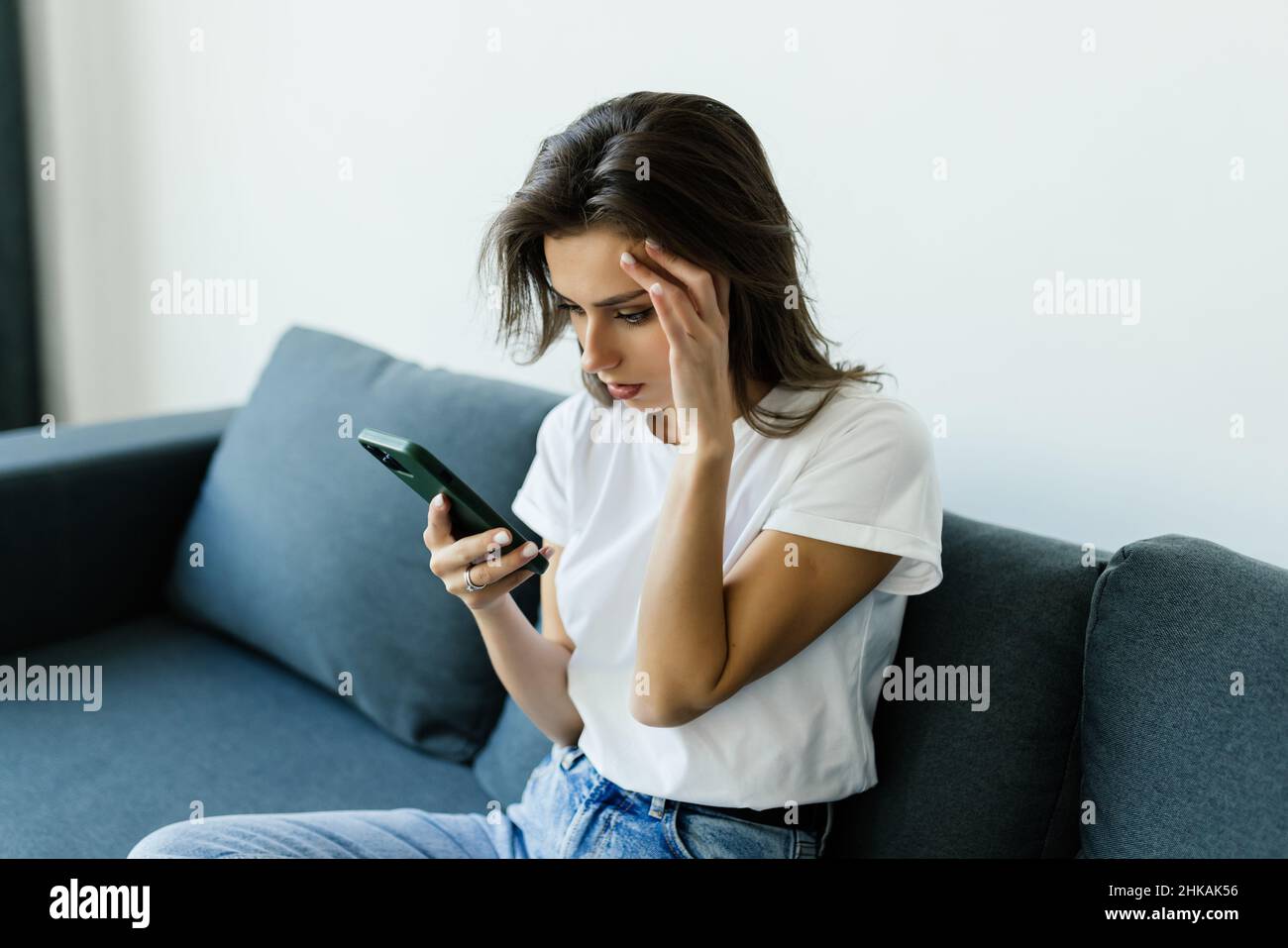 Pensivo sollecitato giovane donna caucasica sedersi sul divano a casa utilizzando il cellulare guardare a distanza pondering del problema. Foto Stock