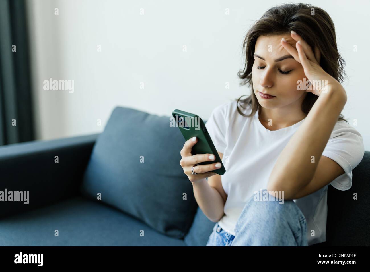 Pensivo sollecitato giovane donna caucasica sedersi sul divano a casa utilizzando il cellulare guardare a distanza pondering del problema. Foto Stock