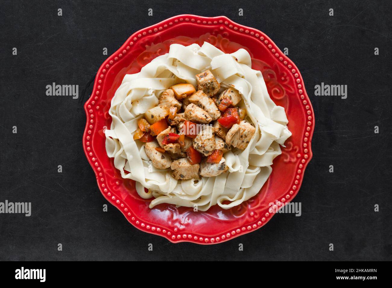 Spaghetti con pollo stufato e verdure su piatto rosso su sfondo nero Foto Stock