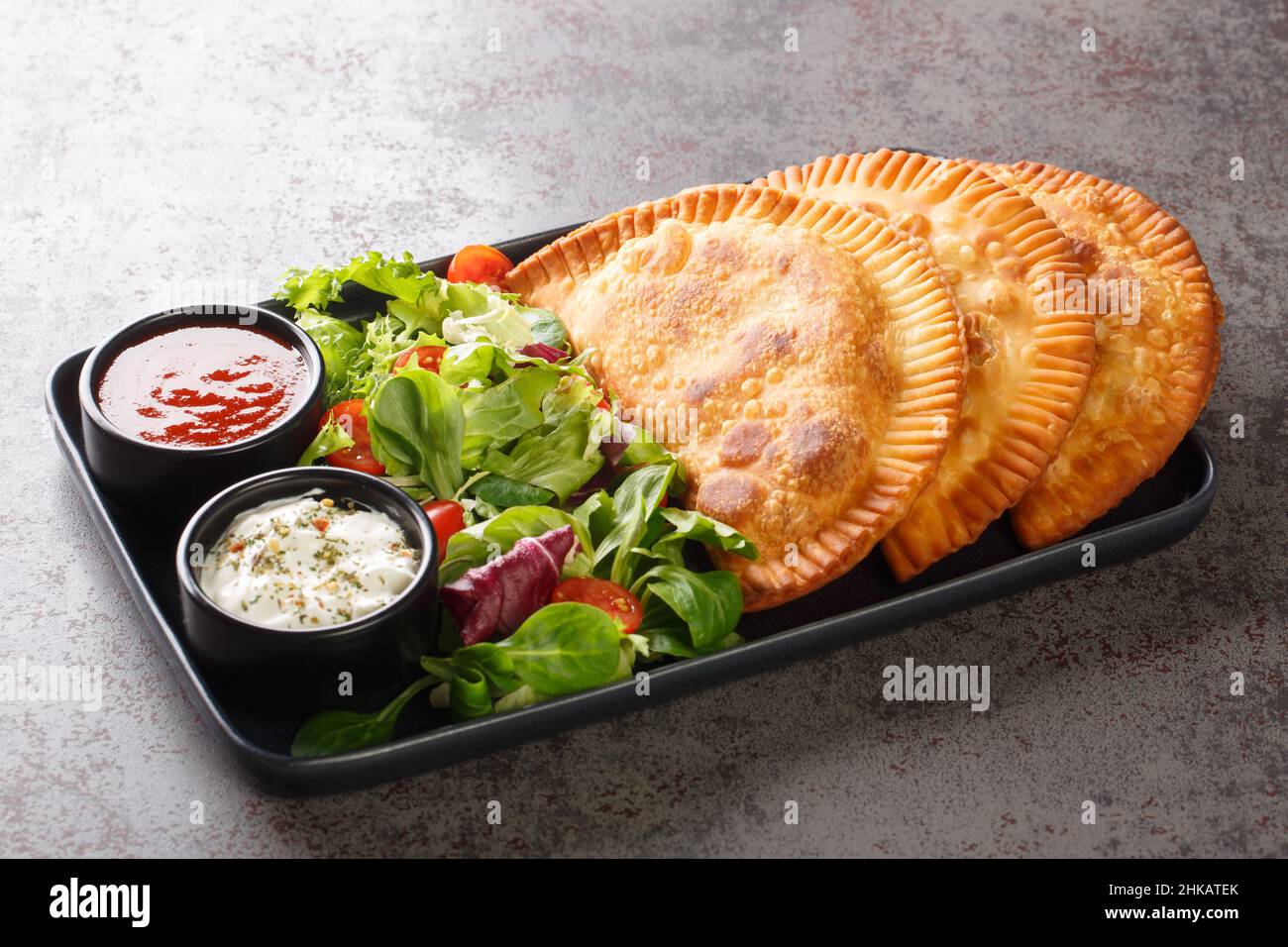 Il Chebureki e' piatto di cucina Tatar Crimea servito con insalata fresca e salse da vicino in un piatto sul tavolo. Orizzontale Foto Stock