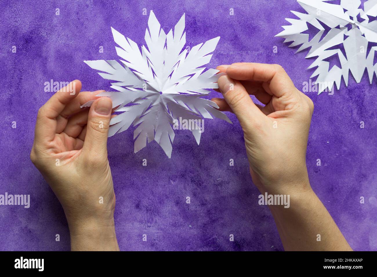 Donna che tiene le mani di carta aperta fiocco di neve sulla superficie viola Foto Stock