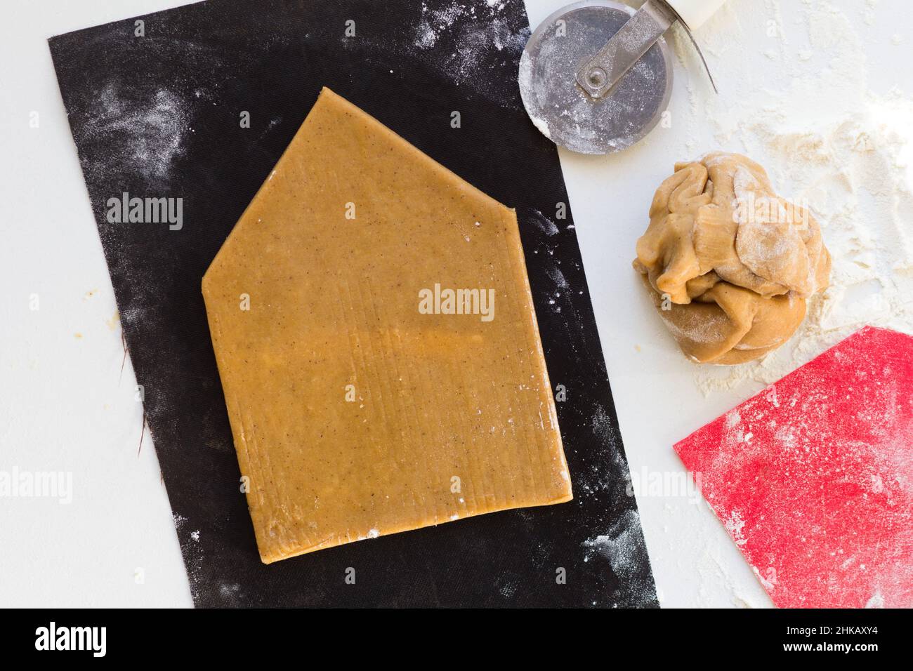 Parete tagliata di casa di pan di zenzero da pasta di pan di zenzero crudo su foglio di teflon nero su sfondo bianco Foto Stock