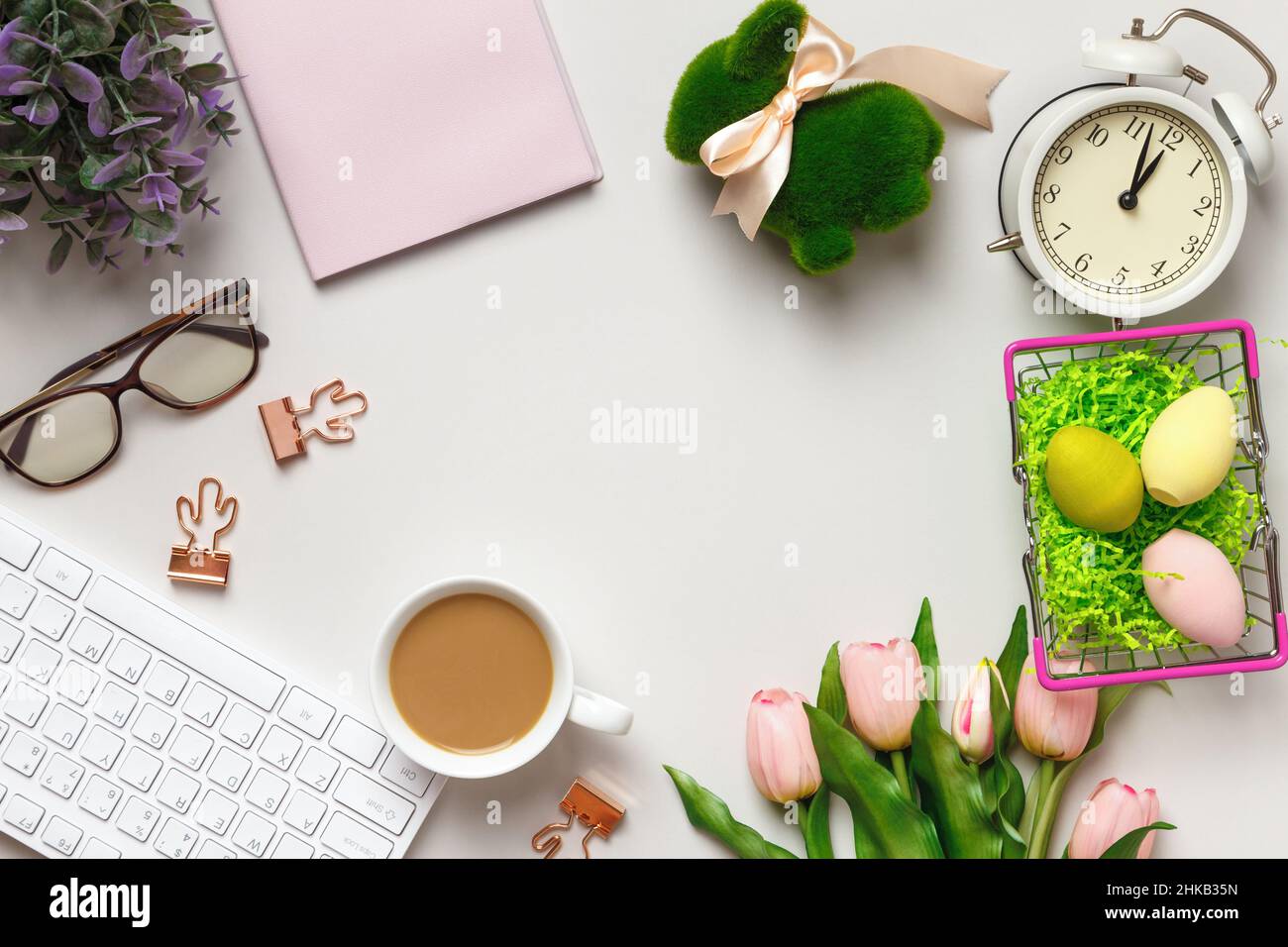 Vista dall'alto del desktop. Tazza di caffè bicchieri tastiera sveglia fiori con decorazioni pasquali. Spazio per la copia di Flat Lay Foto Stock