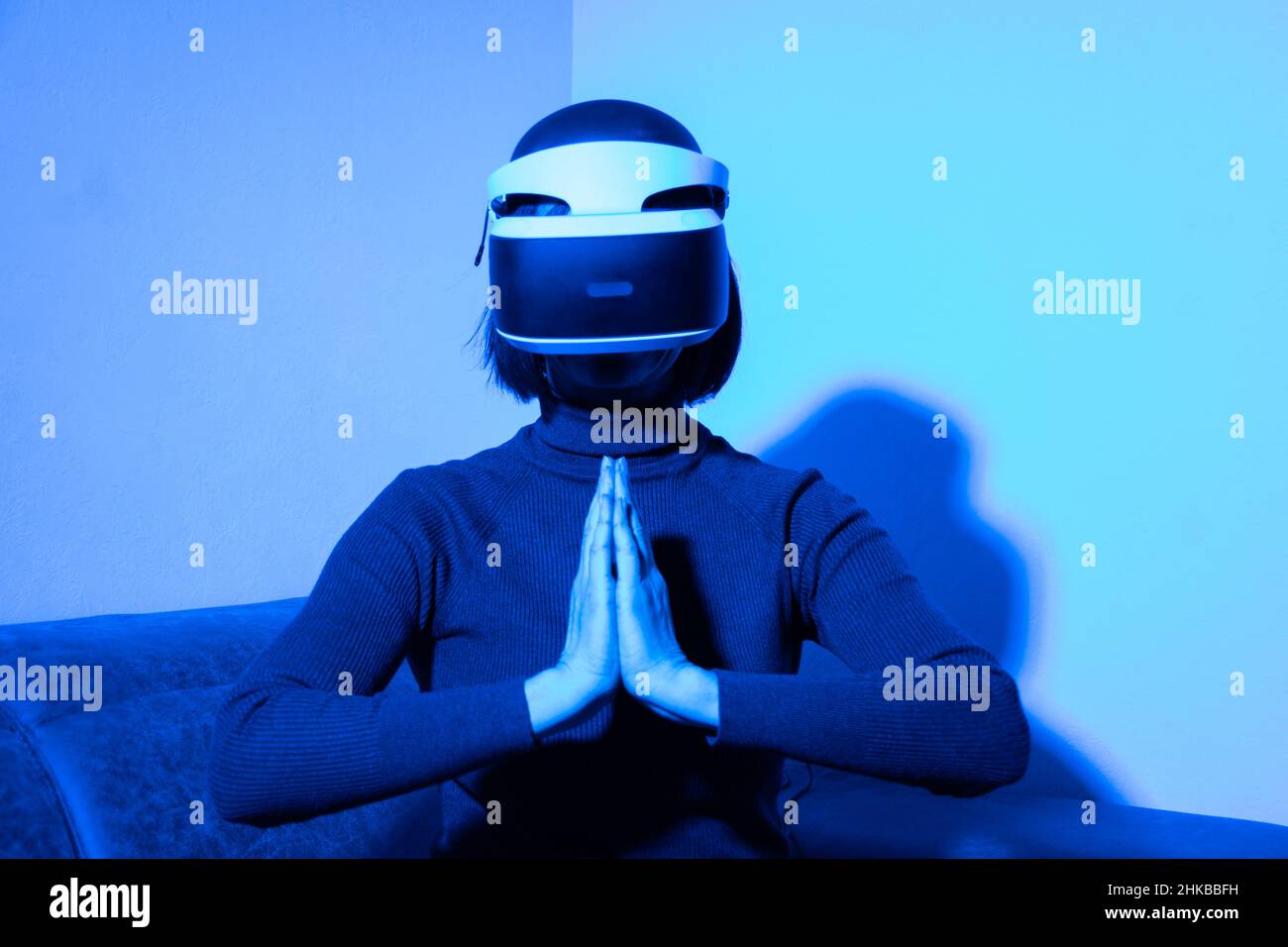 La bella donna che utilizza il visore vr tiene le mani unite nel gesto di preghiera con luce blu. Paga i tuoi rispetti adorando il Buddha. Il concetto di Foto Stock