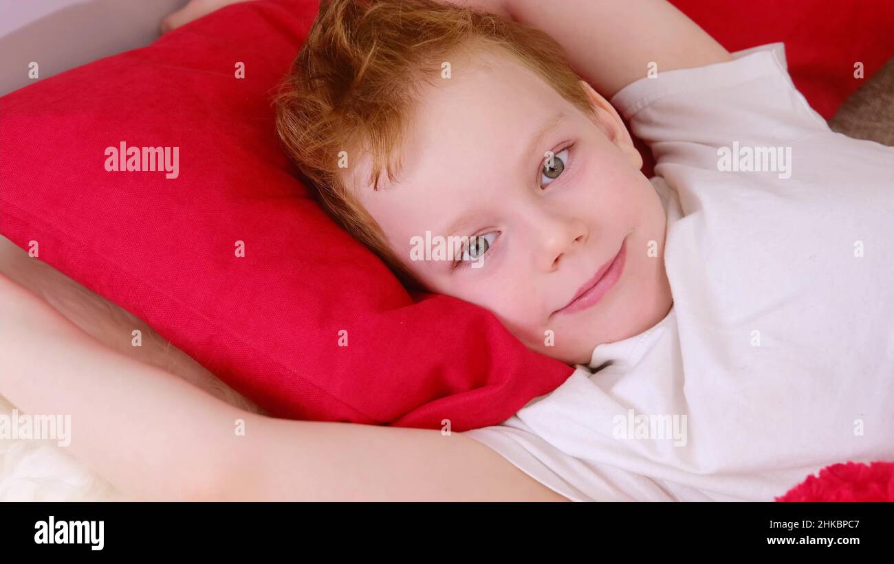 Mattina a letto bambini. Carino divertente ragazzo allegro si sveglia e si trova a letto la mattina, si allunga e sorride. video clip 4k. Relax a letto. Foto Stock