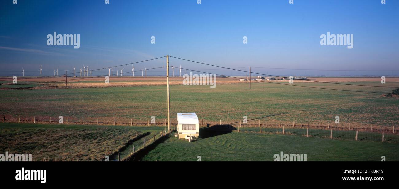 Caravan da solo in angolo di campo da Lydd Road, vicino a Camber Sands sul confine Kent/Sussex. Sullo sfondo si trova la fattoria del vento Little Cheyne Court e il mucca Foto Stock