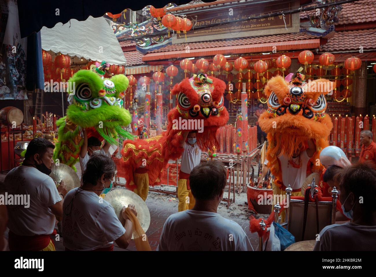 Tre ballerini di leoni e membri della loro troupe si esibiscono fuori da un tempio. Il Capodanno lunare a Bangkok quest'anno è un affare più solenne che negli anni precedenti. Il governo aveva tecnicamente cancellato grandi celebrazioni, ma a Chinatown, una troupe di ballerini di leoni rallentò il traffico in arrivo su Yaowrat Road. Su una strada laterale a Wat Lokanukroh, l'unica eccitazione per il giorno è stato lo scoppio di un piccolo fuoco causato quando le grandi candele rosse illuminate crollarono l'una sull'altra; i custodi si precipitarono per un estintore. Molti Thais di discendenza cinese continuarono a compiere riti e preghiere al santuario undi Foto Stock