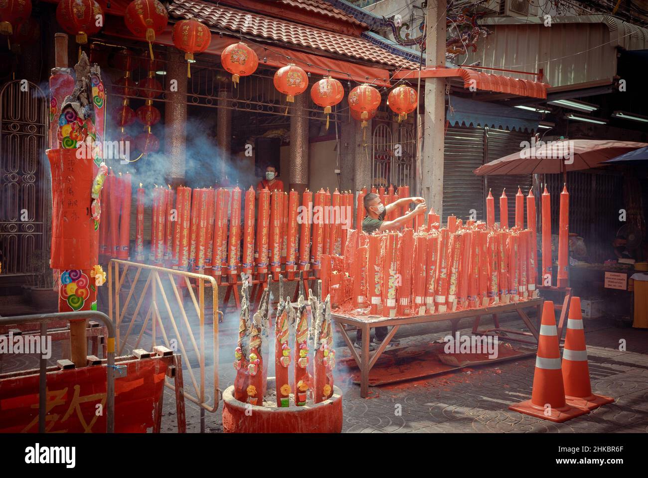 Un custode all'esterno di un tempio illumina un'esposizione di grandi candele rosse. Il Capodanno lunare a Bangkok quest'anno è un affare più solenne che negli anni precedenti. Il governo aveva tecnicamente cancellato grandi celebrazioni, ma a Chinatown, una troupe di ballerini di leoni rallentò il traffico in arrivo su Yaowrat Road. Su una strada laterale a Wat Lokanukroh, l'unica eccitazione per il giorno è stato lo scoppio di un piccolo fuoco causato quando le grandi candele rosse illuminate crollarono l'una sull'altra; i custodi si precipitarono per un estintore. Molti Thais di discendenza cinese continuarono ad eseguire riti e preghiere al santuario undisturbb Foto Stock