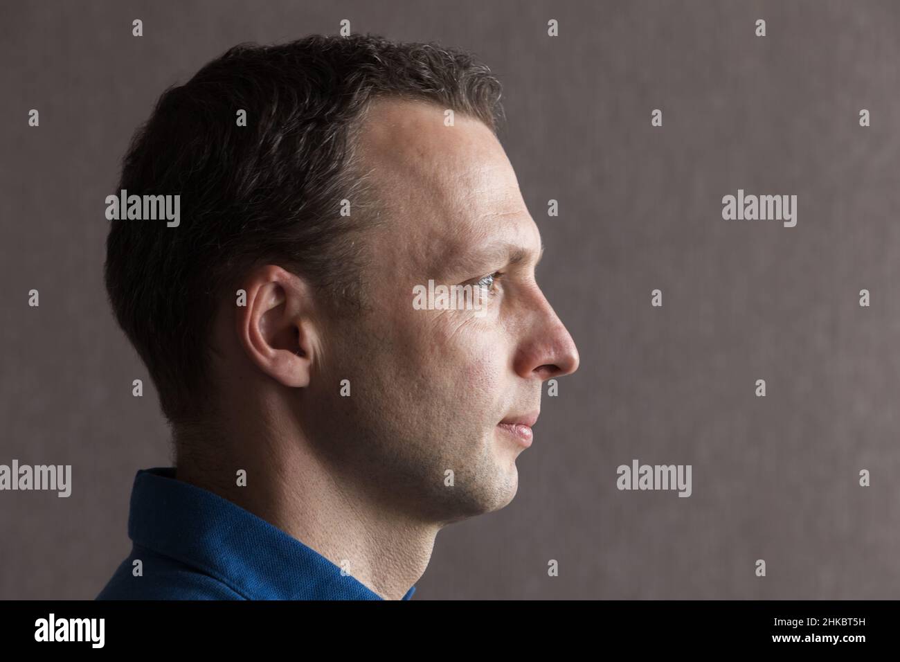 Closeup profilo studio ritratto di giovane adulto europeo uomo su sfondo grigio parete Foto Stock