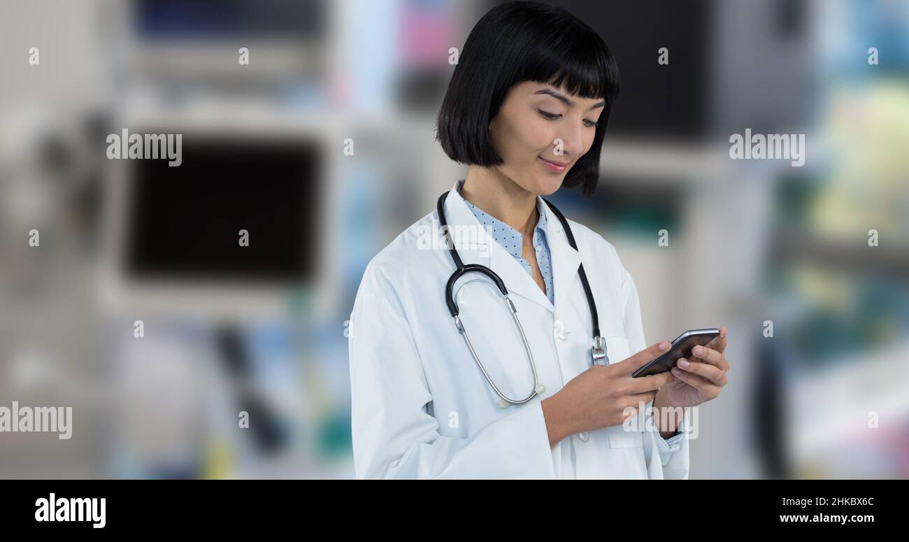 Sorridente medico asiatico giovane donna usando lo smart phone mentre si trova in ospedale Foto Stock