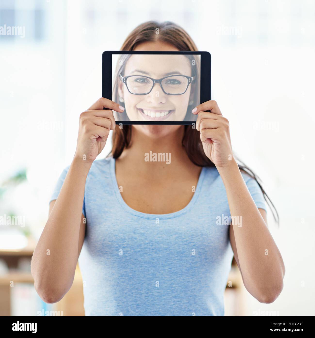 Il volto della tecnologia moderna. Una giovane donna che tiene un tablet digitale con uno schermo trasparente davanti al suo volto. Foto Stock
