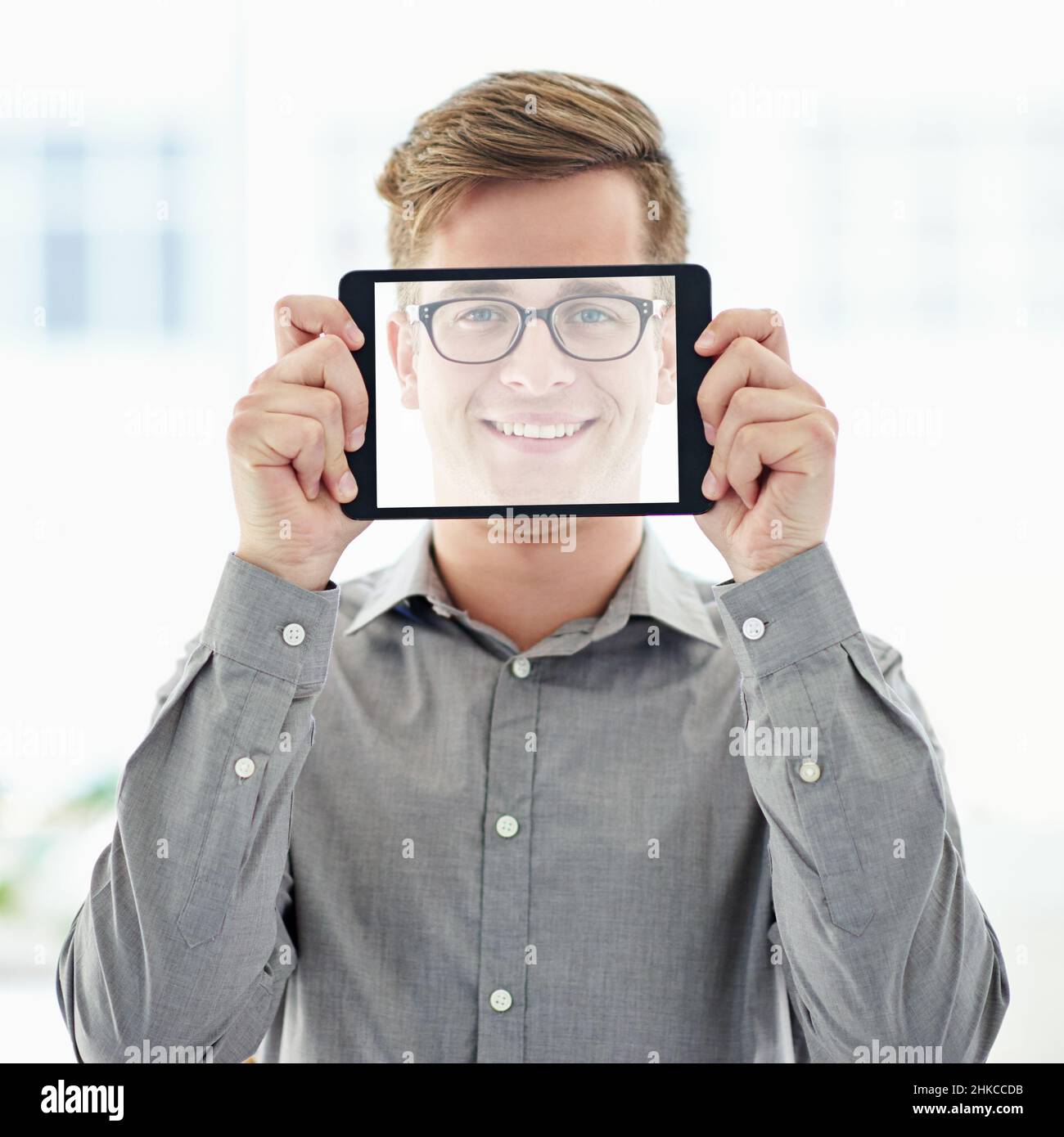 Tecnologia per me e per te. Un giovane uomo che tiene un tablet digitale con uno schermo trasparente davanti al suo volto. Foto Stock