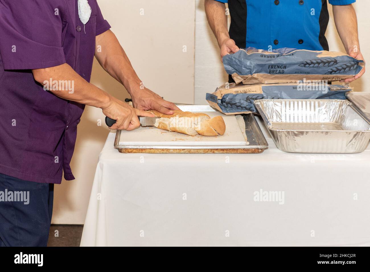 Mani forti che affettano il pane francese in porzioni uguali per tutti gli ospiti della festa. Foto Stock