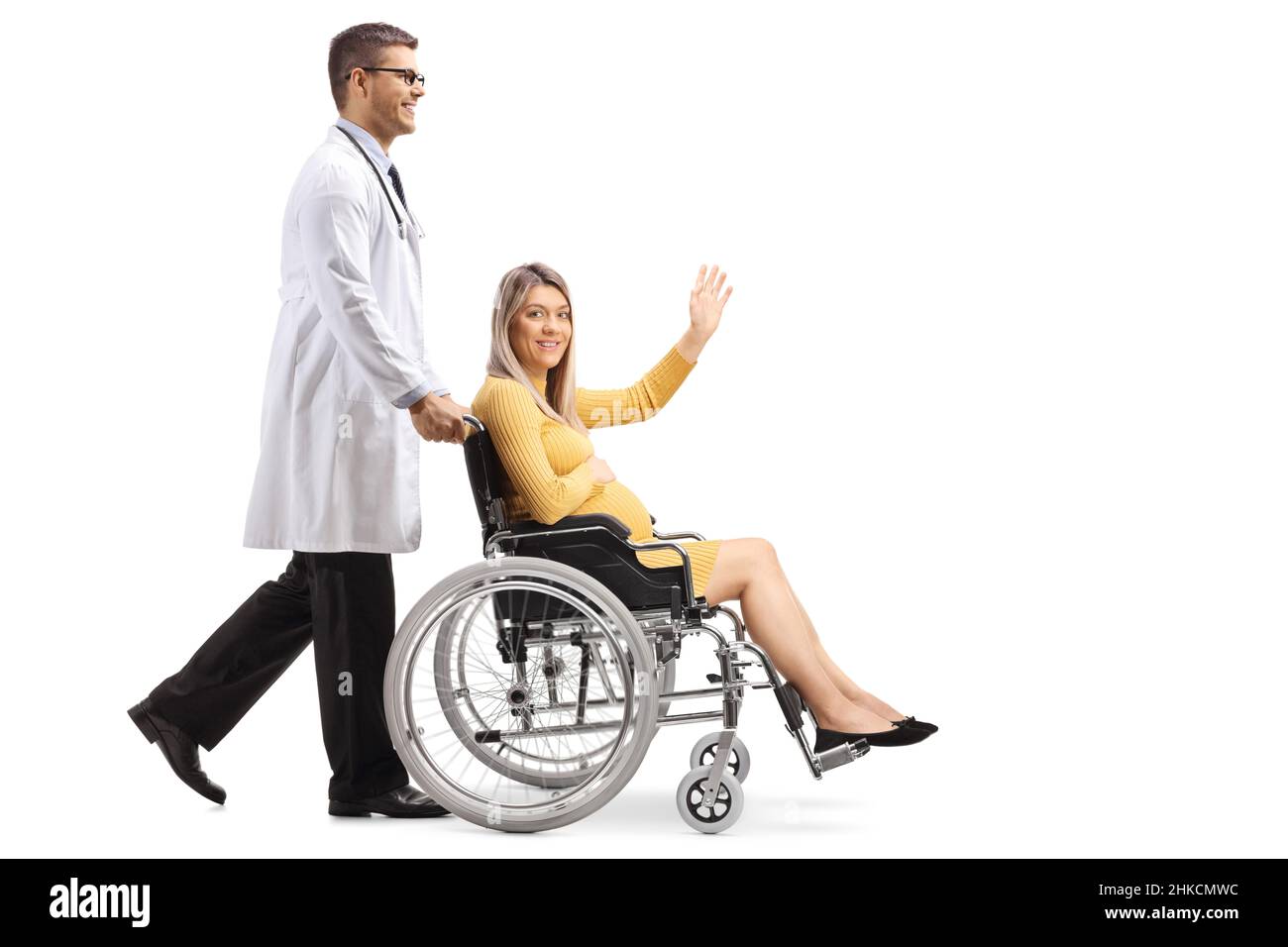 Colpo di profilo a tutta lunghezza di un medico che spinge una donna incinta seduta su una sedia a rotelle e che agita isolato su sfondo bianco Foto Stock