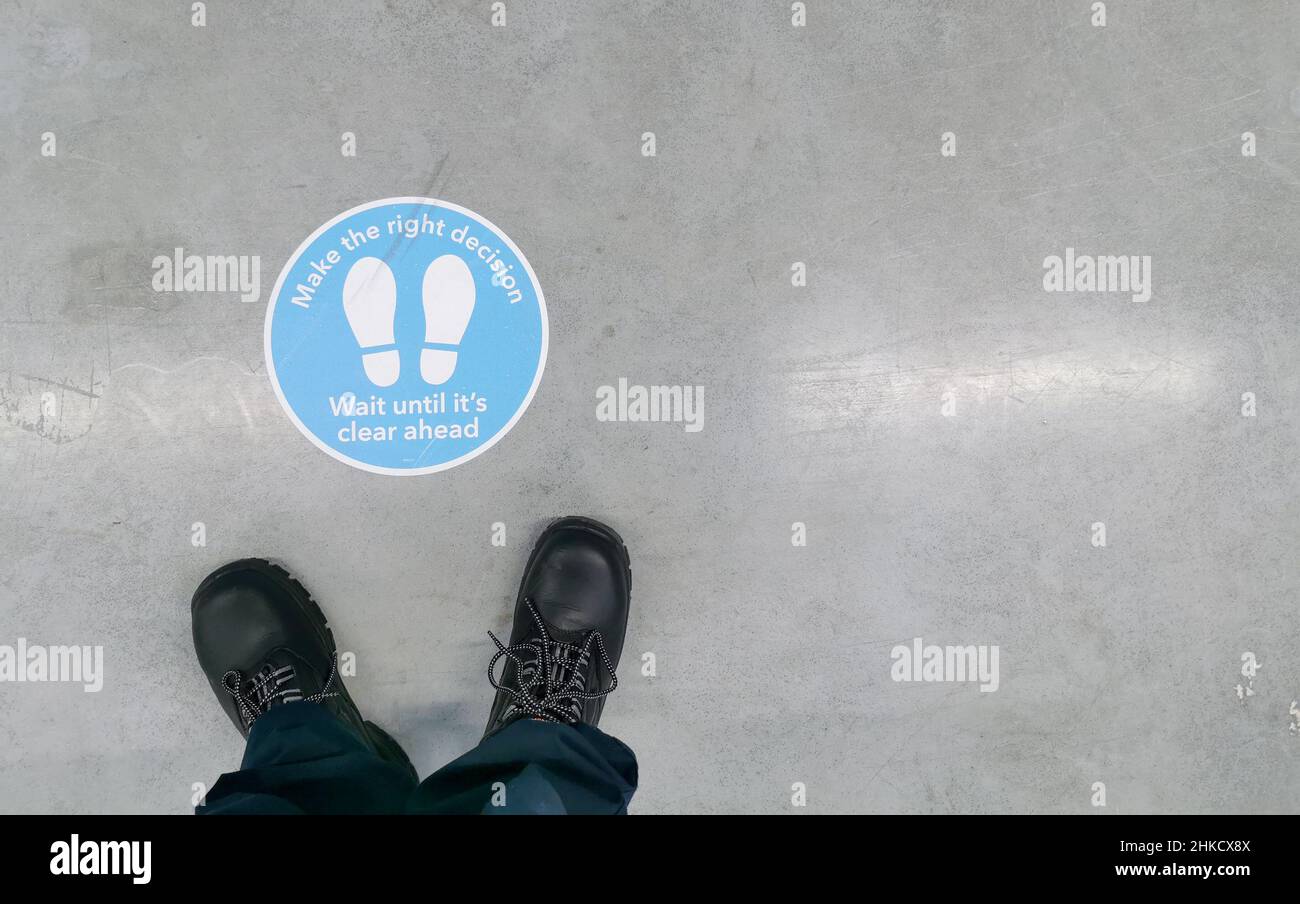 Segnaletica per consigliare di mantenere la distanza visibile sul pavimento di un magazzino con stivali di sicurezza davanti ad esso. Foto Stock