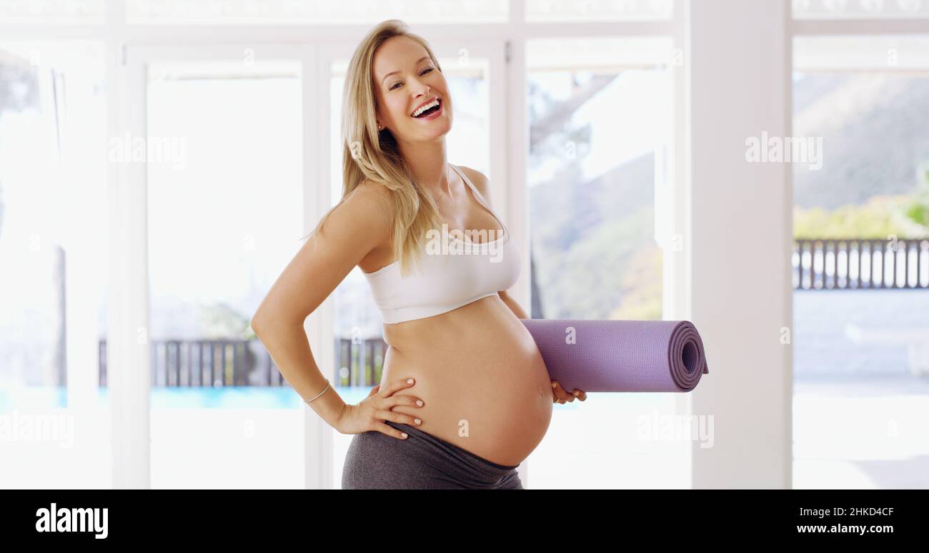 Divertirsi con il fitness. Ritratto corto di una giovane donna incinta attraente che porta un tappeto yoga. Foto Stock