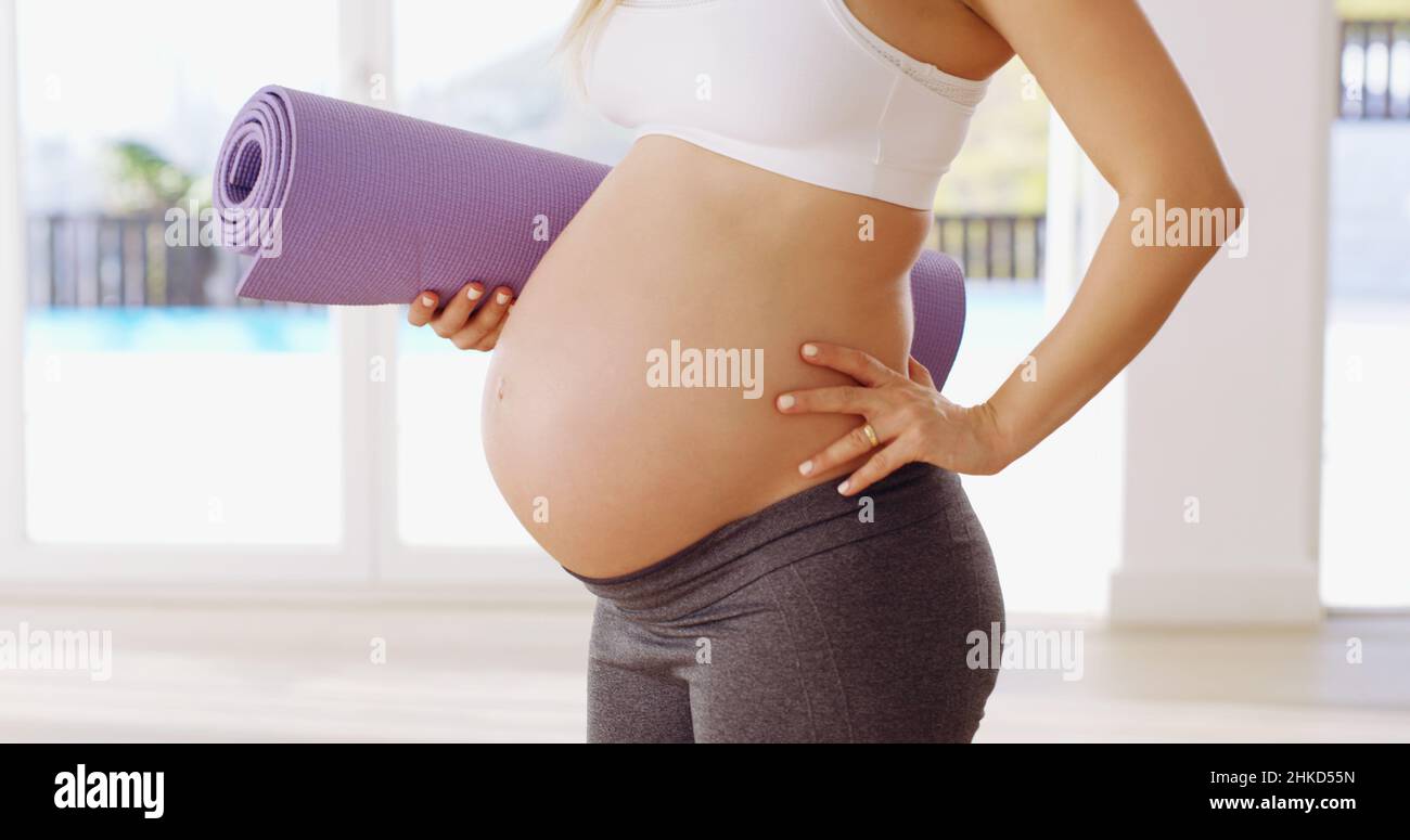 Mostrando fuori il suo bump del bambino. Scatto corto di una giovane donna incinta irriconoscibile che porta un tappeto yoga. Foto Stock