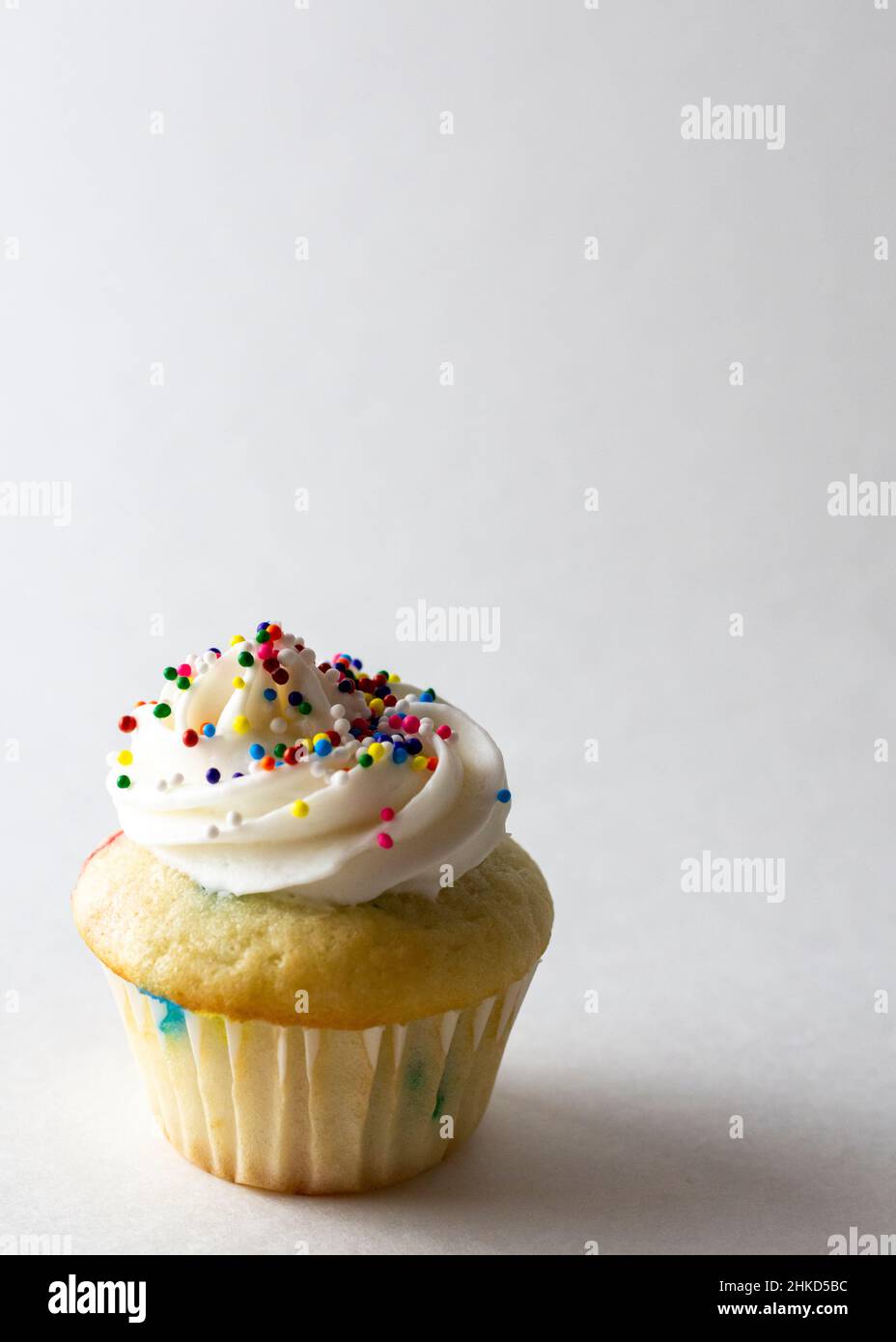 Vista ravvicinata di un mini cupcake decorato con mini spolverini di caramelle color primavera. Sfondo bianco con spazio di copia. Foto Stock