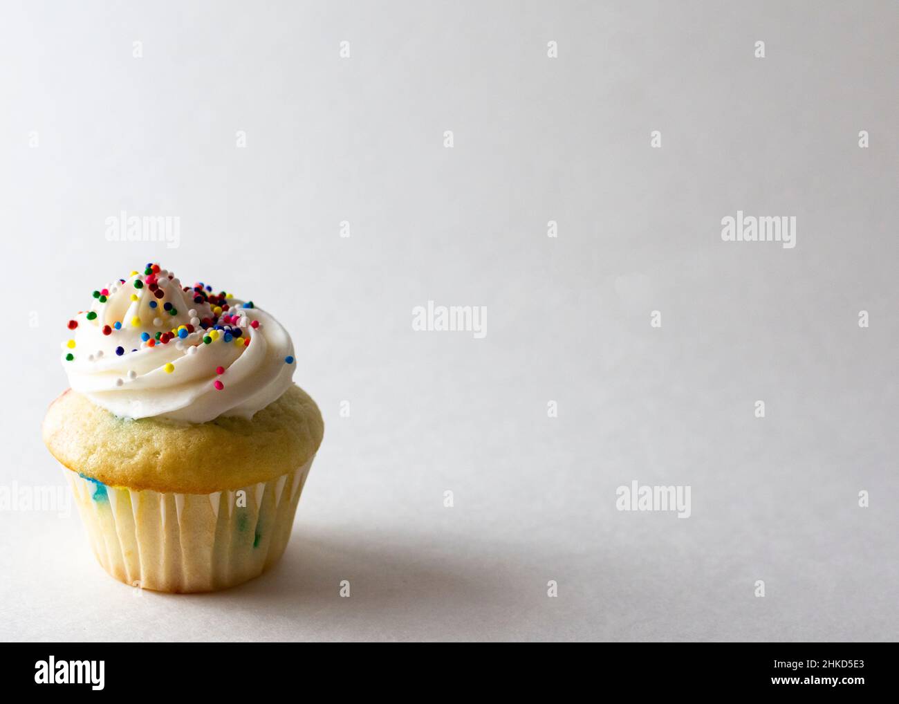 Vista ravvicinata di un mini cupcake decorato con mini spolverini di caramelle color primavera. Sfondo bianco con spazio di copia. Foto Stock