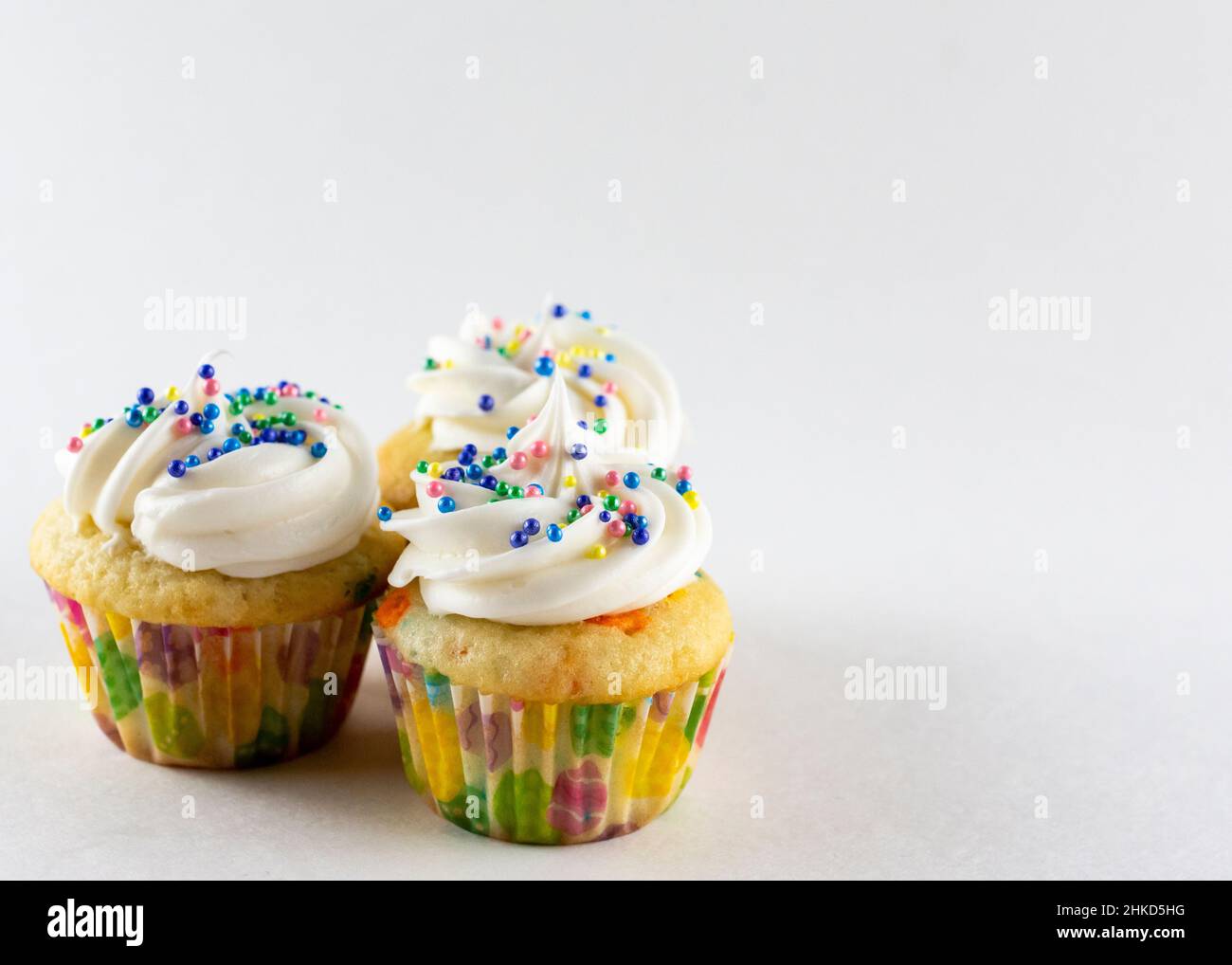Tre mini cupcake a confetti su sfondo bianco. Decorato con spolverini pasquali. Spazio di copia. Foto Stock