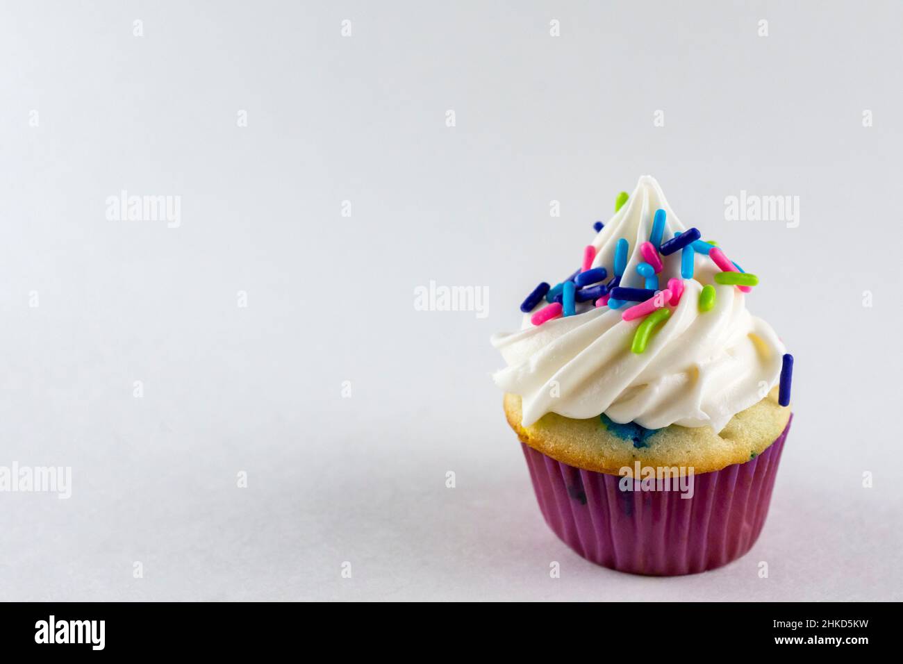 Vista ravvicinata di un mini cupcake decorato con spolverini di caramelle color primavera. Sfondo bianco con spazio di copia. Foto Stock