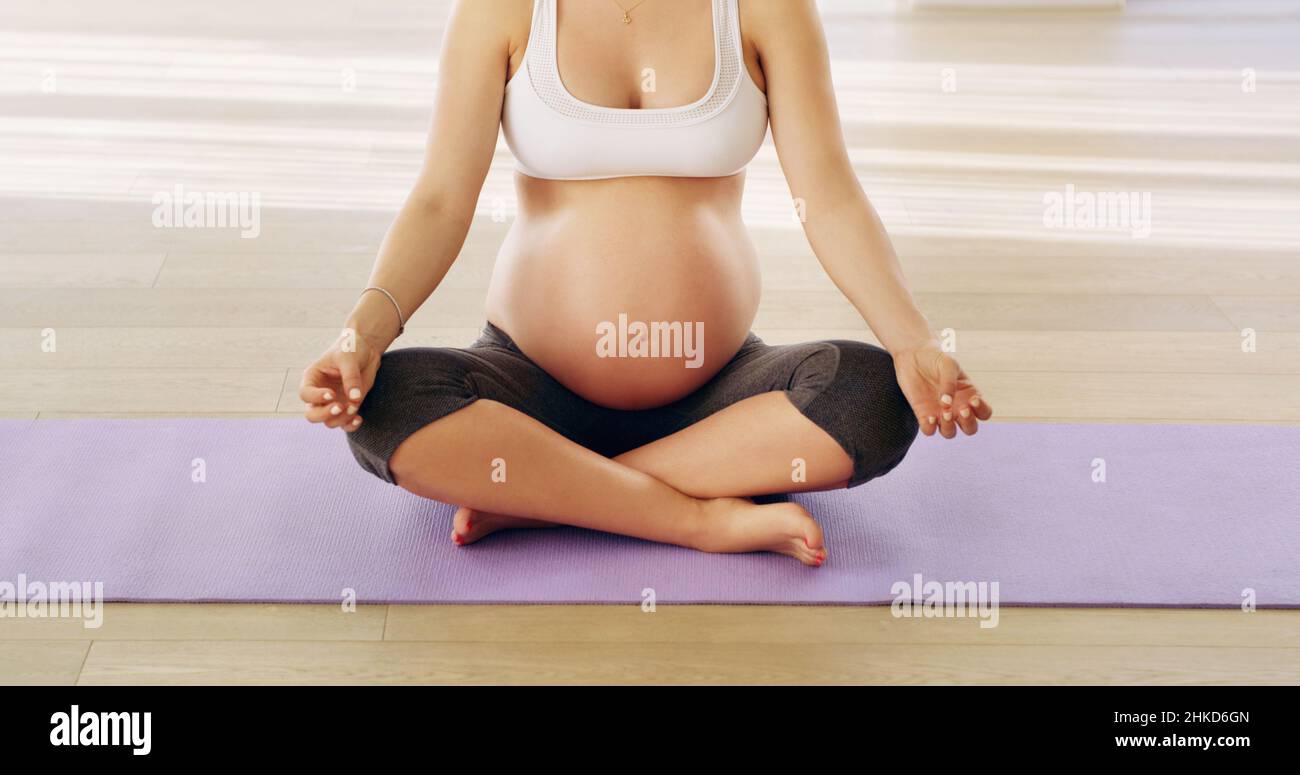 Equilibrando la sua nuova vita. Scatto corto di una giovane donna incinta irriconoscibile meditando su un tappeto yoga. Foto Stock