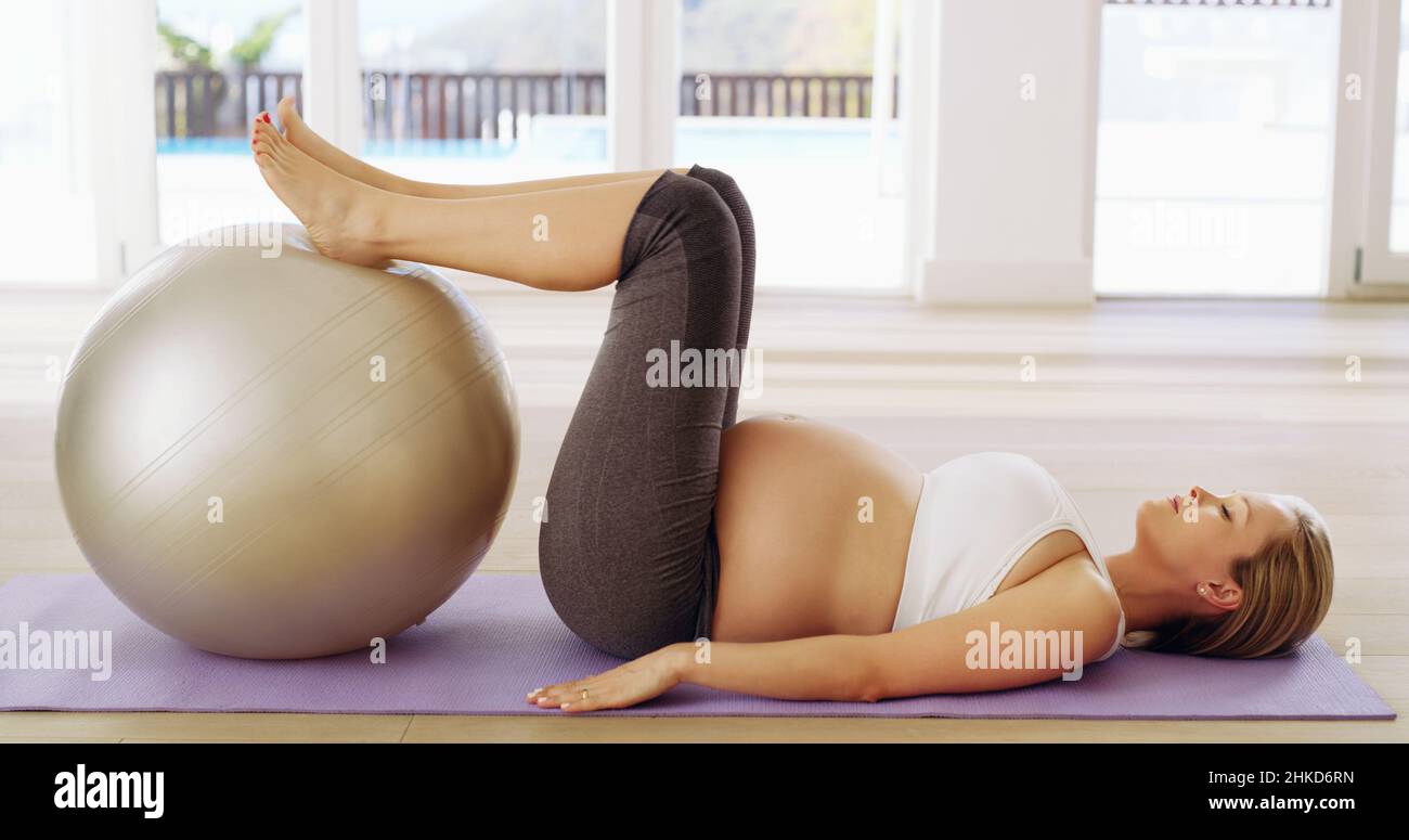Fare un allenamento prenatale. Scatto a tutta lunghezza di una giovane donna incinta attraente che si sta allenando con una sfera di esercitazione. Foto Stock
