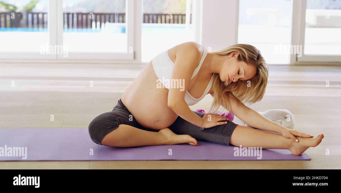 Per il bambino è sempre più sobrio. Scatto a tutta lunghezza di una giovane donna incinta attraente che si riscalda prima di un allenamento. Foto Stock