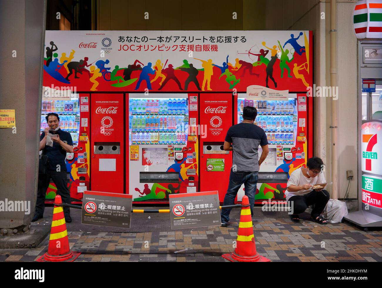 tokyo, giappone - agosto 30 2021: Uomini giapponesi che mangiano i fast food del konbini di fronte ad un distributore automatico di bevande avvolto con vettori raffiguranti sil sport Foto Stock