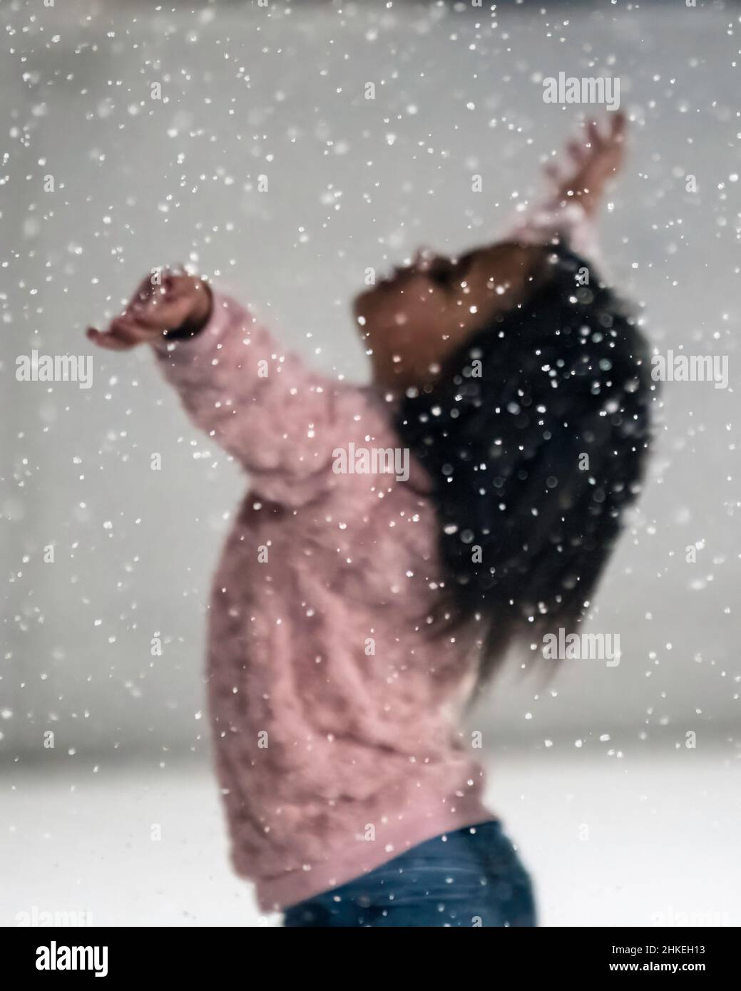 Prattville, Alabama, USA- 23 dicembre 2021: Focus sui fiocchi di neve con una giovane ragazza che solleva le mani in aria fuori fuoco in background Foto Stock