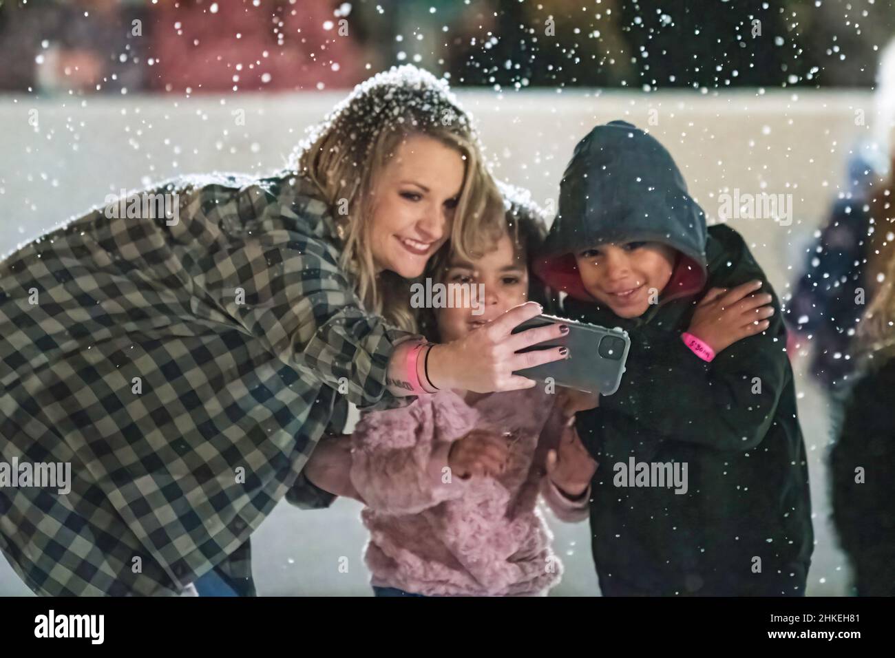 Prattville, Alabama, USA- 23 dicembre 2021: Una donna si pone con una giovane ragazza e ragazzo nella neve artificiale mentre prende un selfie sul suo telefono al Foto Stock