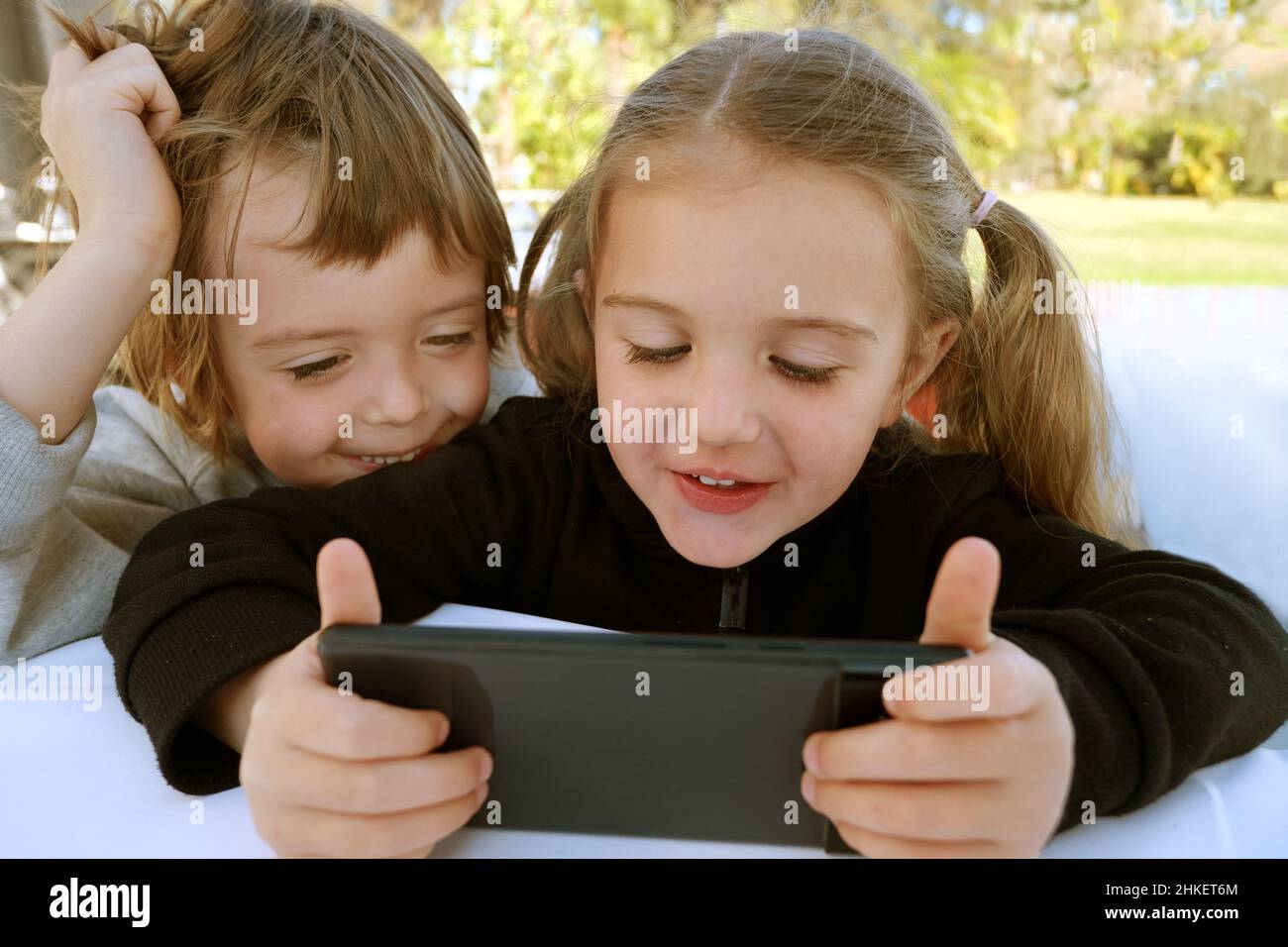 Little boy and girl simpatiche fratelli e sorelle usando gli smart phone che giocano con videogiochi, guarda i cartoni animati discutere di nuove divertenti applicazioni mobili, divertendosi la settimana Foto Stock