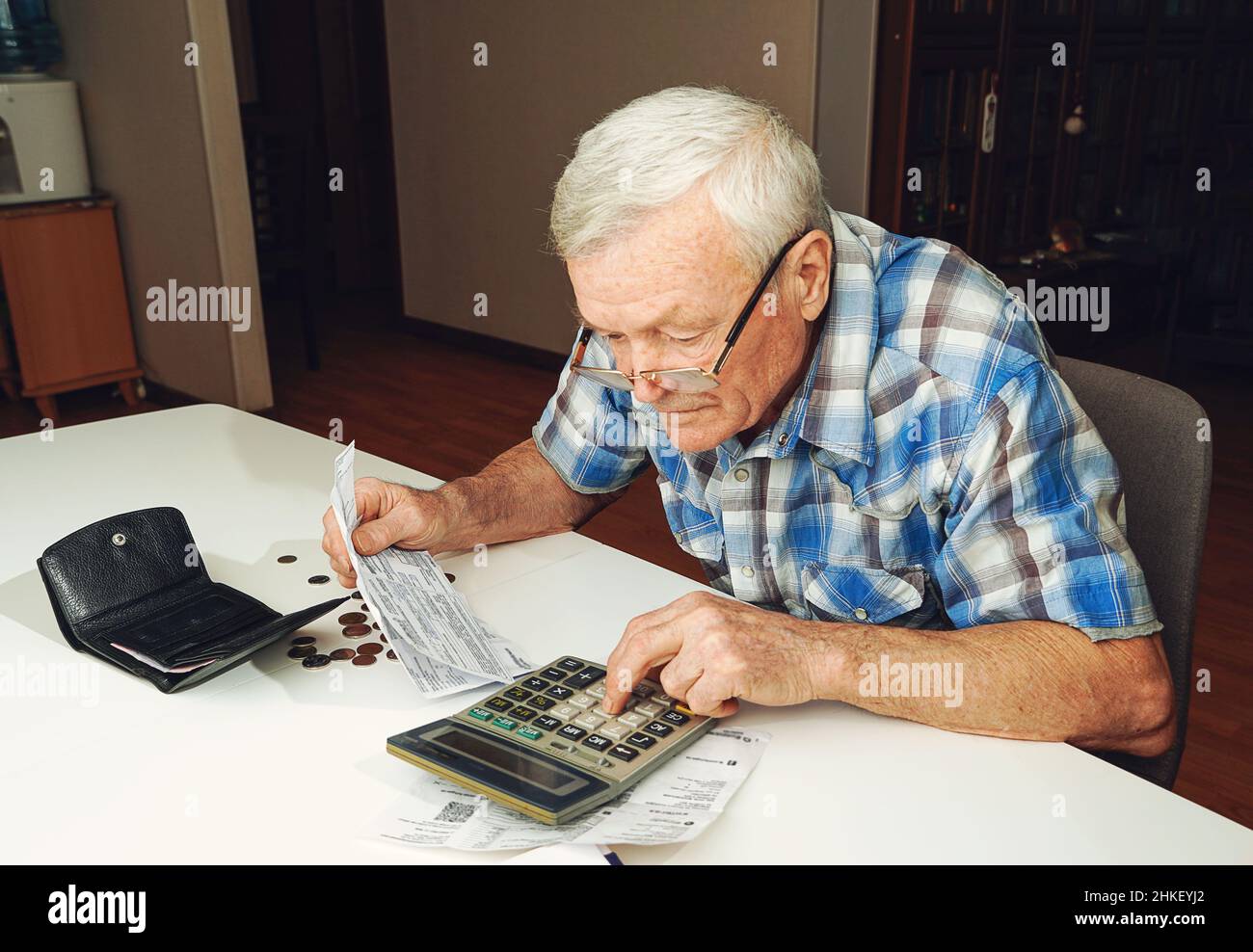 Sconvolto uomo anziano seduto al tavolo e calcolando le finanze. Vecchio controllo fatture. Uomo che conta le monete sul tavolo. Concetto di calcolo della pensione Foto Stock