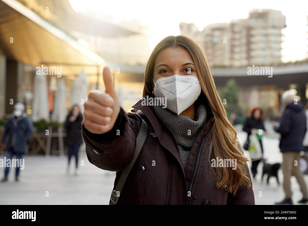 Pollice su donna indossando maschera protettiva e vestiti invernali in città Foto Stock