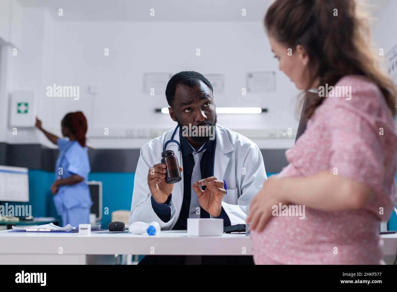 Medic afroamericano che dà una bottiglia di pillole a persona incinta per curare la malattia. Pallone di tenuta del medico con medicinale da prescrizione e trattamento da somministrare a una donna in gravidanza. Foto Stock