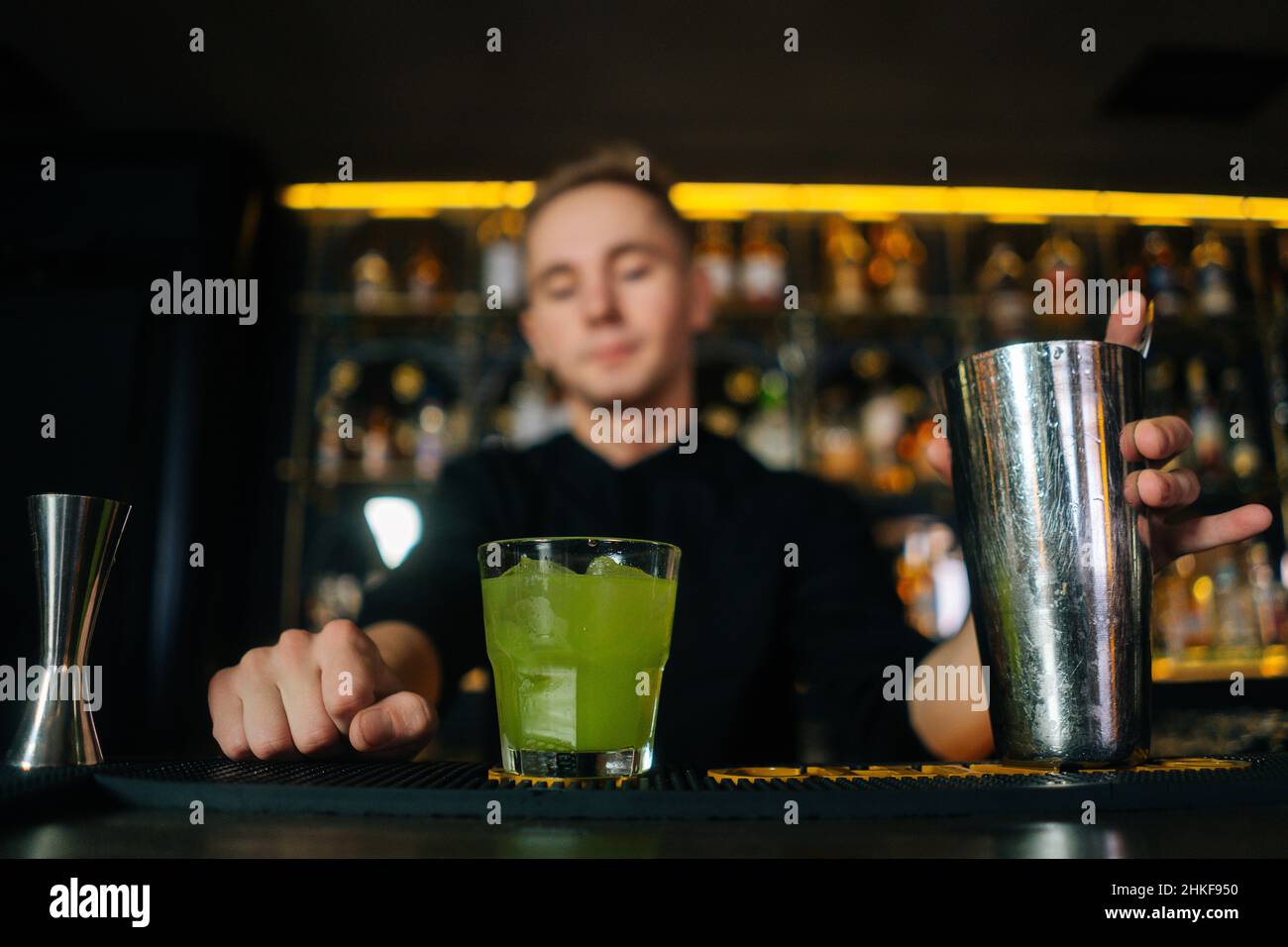 Vista ravvicinata dal basso angolo del fidato barman maschio che offre un cocktail pronto al cliente che si trova dietro il bancone del bar nel moderno nightclub. Foto Stock