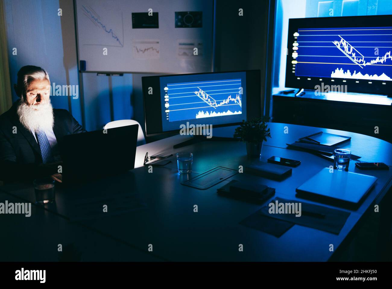 Uomo d'affari anziano che lavora di notte all'interno dell'ufficio dell'azienda del fintech - fuoco morbido sul fronte maschio Foto Stock