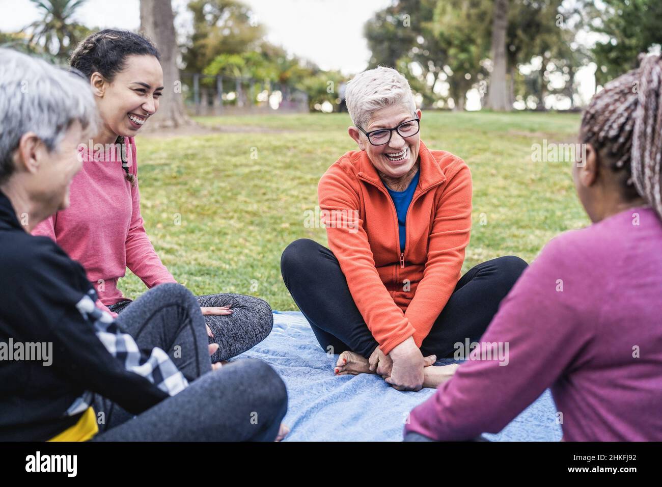 Happy donne multi generazionali divertirsi insieme seduti all'aperto al parco della città - Focus principale sulle braccia del centro senior femminile Foto Stock