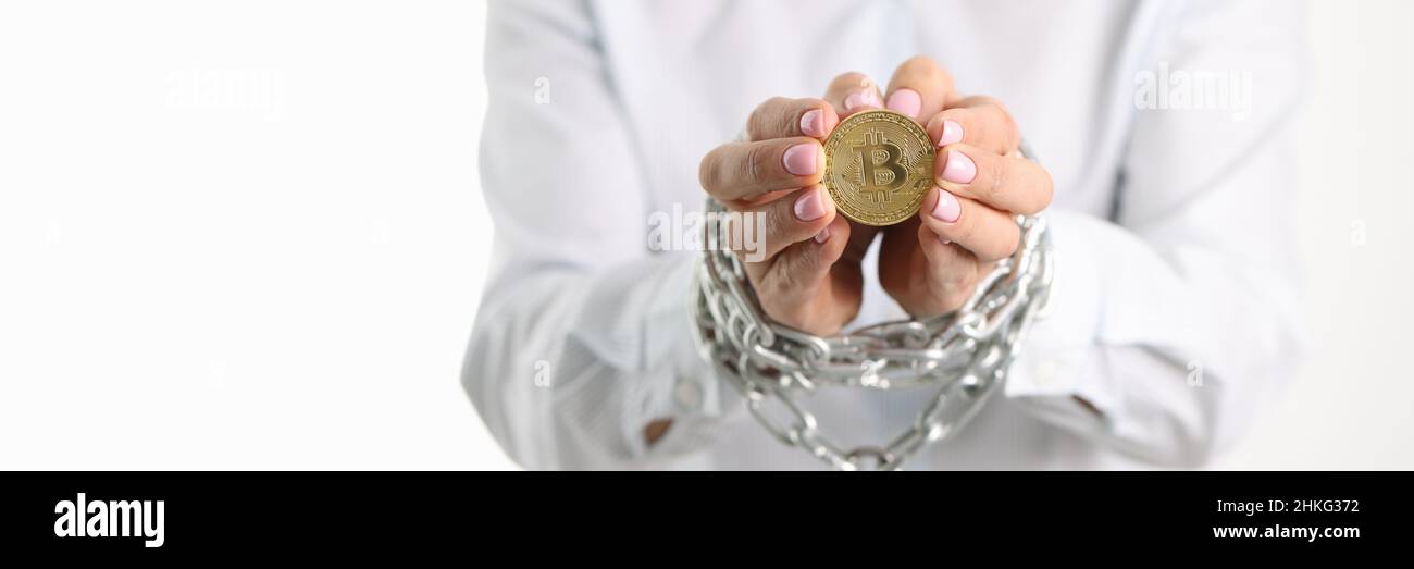 Donna con le mani legate della catena di metallo che tiene il closeup della moneta di bitcoin Foto Stock