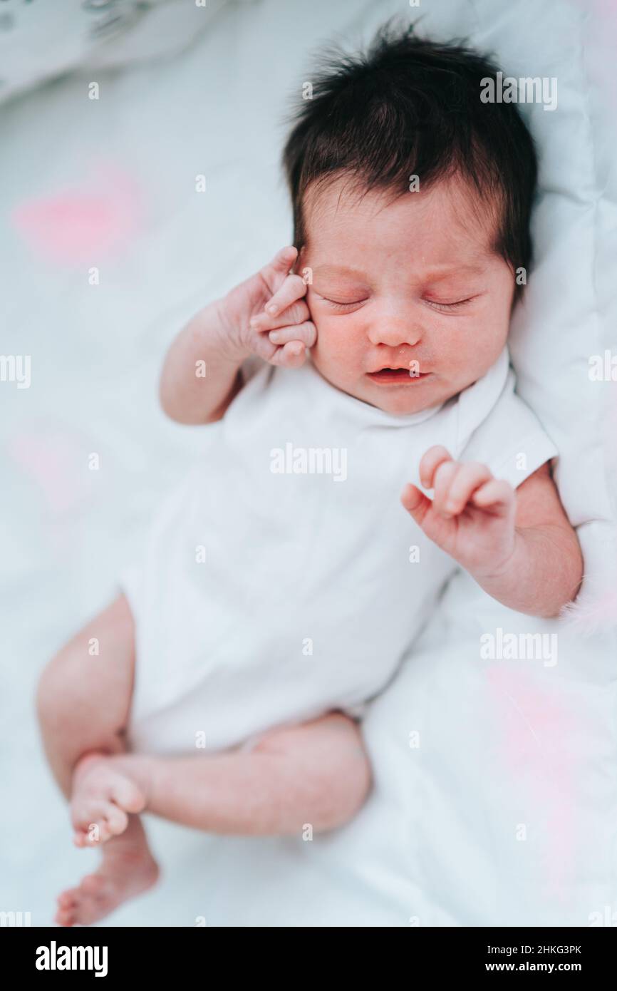 Fantastico neonato con corti capelli scuri in bodysuit bianco che dorme sulla schiena mescolando in DREAM su coperta bianca.Vertical Foto Stock