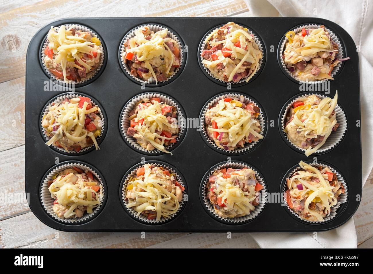 Vassoio da forno con muffin per pizza preparati e sostanziosi da pasta di lievito, pomodori, verdure, salsiccia e formaggio pronti per il forno, vista ad angolo alto da abo Foto Stock