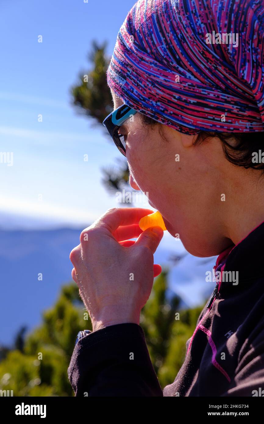 Donna che mangia un cuneo d'arancia come rinfresco sulla cima di una montagna Foto Stock