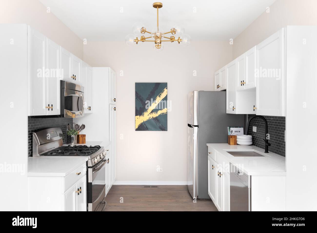 Una bella cucina con armadietti bianchi, ripiani in marmo, backsplash in piastrelle di marmo nero della metropolitana, e una luce dorata appesa sopra. Foto Stock