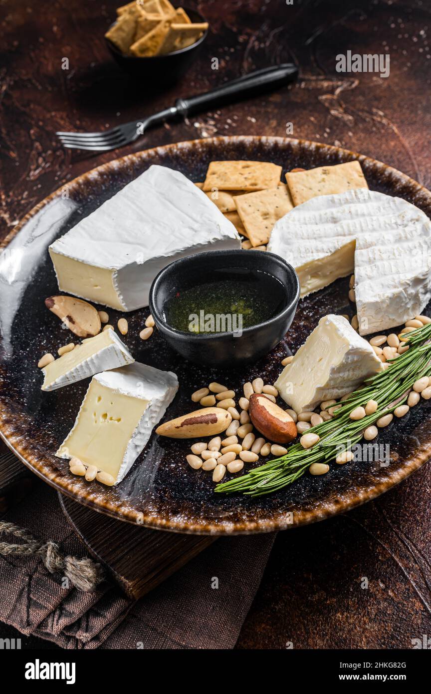 Piatto di formaggi con brie e camembert su piatto rustico con noci e miele. Sfondo scuro. Vista dall'alto Foto Stock